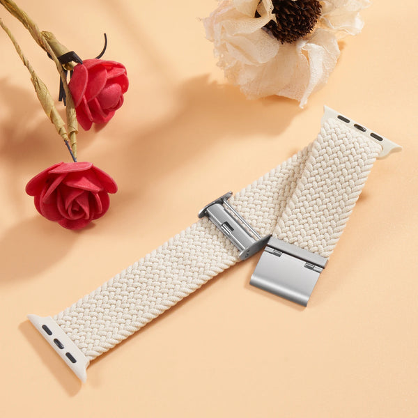 A beige braided stretch band for an Apple Watch is displayed next to red roses and a dried flower.