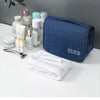 Un sac organisateur en tissu bleu marine avec divers produits de soins de la peau et de beauté sur une surface blanche.