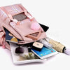A pink canvas backpack with a plaid pattern and a fluffy pink pom-pom, next to a smartphone.