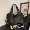 A black punk rivet leather tote bag resting on a dark surface next to a framed poster.