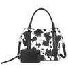 A black and white cow print faux leather tote bag with a black clutch attached.