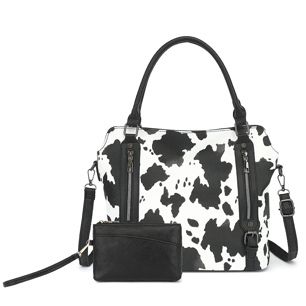 A black and white cow print faux leather tote bag with a black clutch attached.