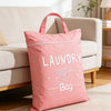 A pink laundry bag with a handle is placed on a light-colored floor in a bright living room setting.