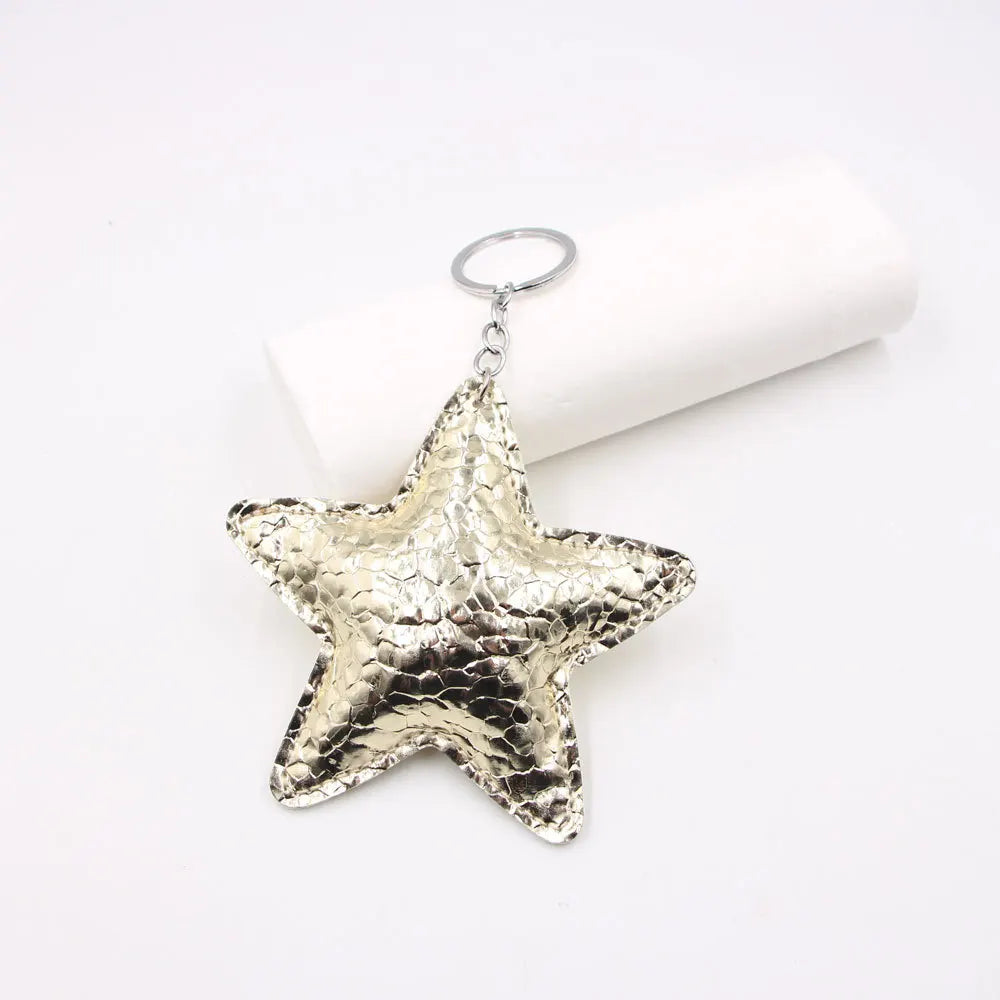 A shiny gold star-shaped leather key chain pendant hanging from a silver keyring.