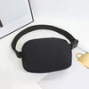 A black nylon cross-body waist bag is shown resting on a white surface next to a piece of paper.