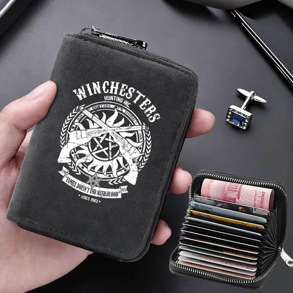 A black zippered card wallet featuring a hunting insignia design is held in a hand next to a stack of credit cards.