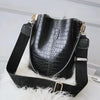 Black vintage alligator pattern leather crossbody bag with black strap resting on white fur
