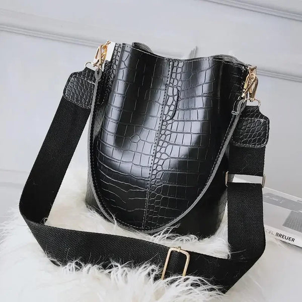 Black vintage alligator pattern leather crossbody bag with black strap resting on white fur