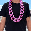 A man wearing a chunky pink acrylic Cuban link necklace around his neck.
