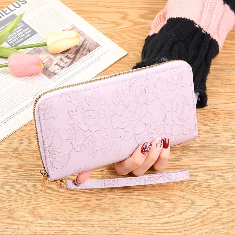 Cartera de cuero PU rosa con estampado floral, sobre una superficie de madera junto a una mano y un tulipán verde