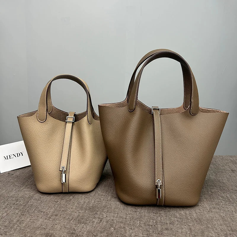 A tan genuine leather bucket bag with a zipper closure is displayed on a gray surface.