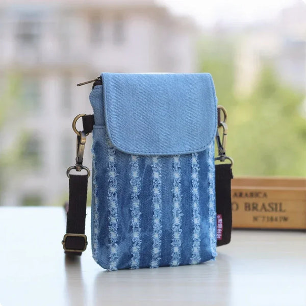 A light blue denim mini messenger bag with black straps resting on a white surface.