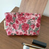 A pink floral cosmetic pouch with a red rose pattern rests on a wooden surface next to a makeup brush.