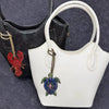 White leather handbag with a gold strap and a colorful beaded charm