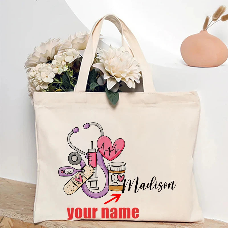 A beige canvas tote bag featuring a pink heart, stethoscope, and the name Madison with space for a personalized name.