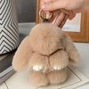 A light tan plush rabbit fur keychain with gold hardware being held by a hand.