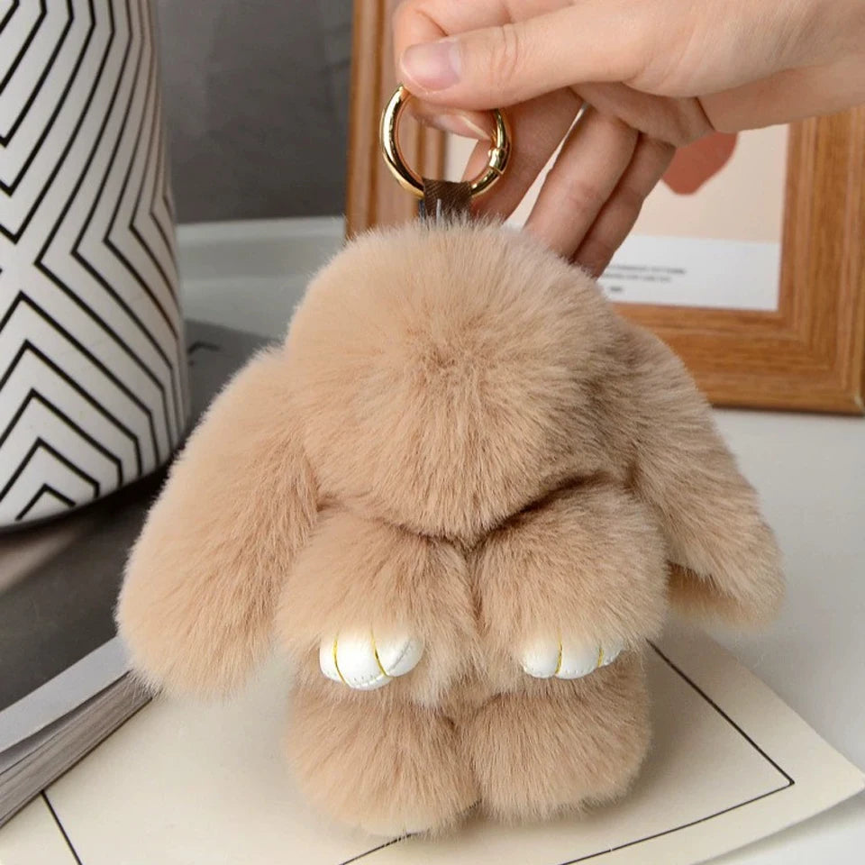 A light tan plush rabbit fur keychain with gold hardware being held by a hand.