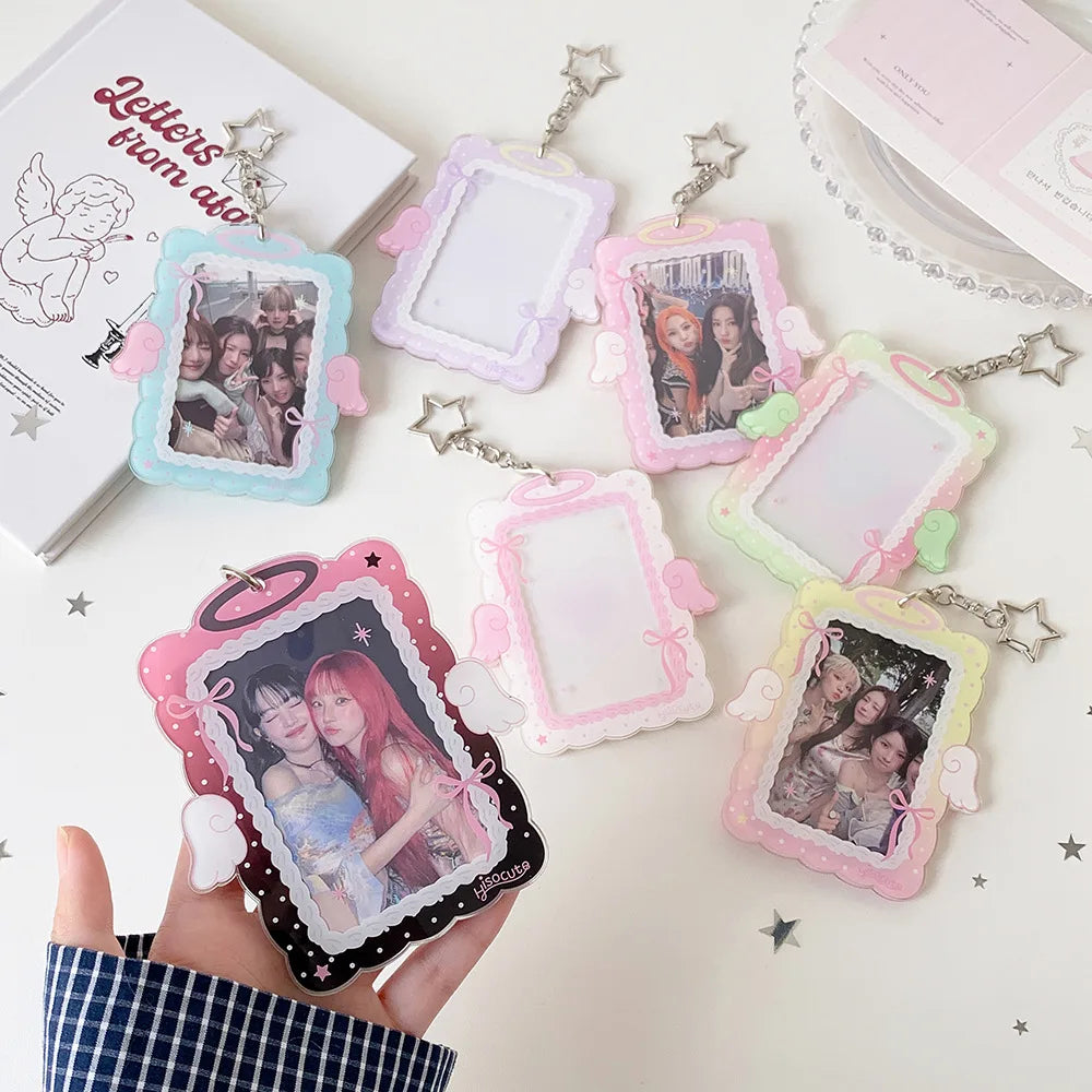 A hand holds several angel wings photocard holders with clear display cases in various pastel colors