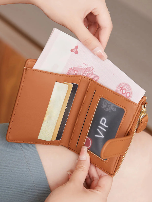 A hand is opening a brown PU leather bifold wallet with a zipper closure, revealing cards and cash.
