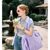 A woman wearing sunglasses and a striped shirt holds a purple tote bag outdoors.