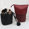 A maroon makeup brush storage case with a black brush holder and a separate brush brush.