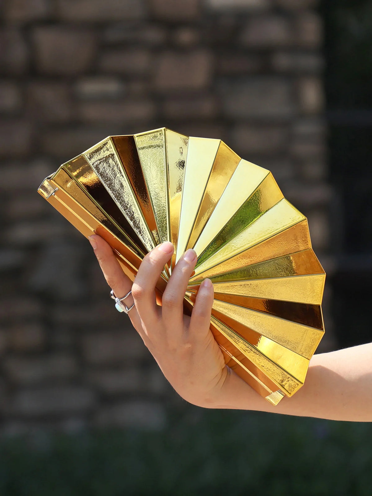 A hand holds a gold acrylic chain crossbody bag with multiple layered, reflective panels.