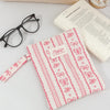 A pink floral plaid cotton tablet pouch with a secure closure rests next to eyeglasses and a notebook.