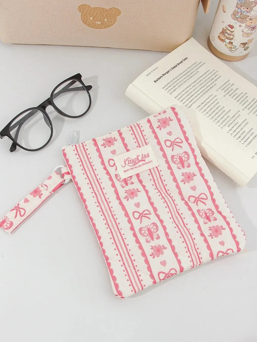 A pink floral plaid cotton tablet pouch with a secure closure rests next to eyeglasses and a notebook.