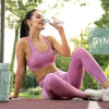 A woman in pink athletic wear is sitting on a red surface with a gym bag for women nearby.