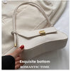 A light beige leather crossbody bag with gold hardware shown being held by a hand.