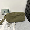 A olive green cotton canvas shoulder crossbody bag resting on a gray surface next to a digital clock and some printed materia