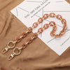 A delicate pink acrylic chain necklace laid on a brown fabric next to a piece of paper.