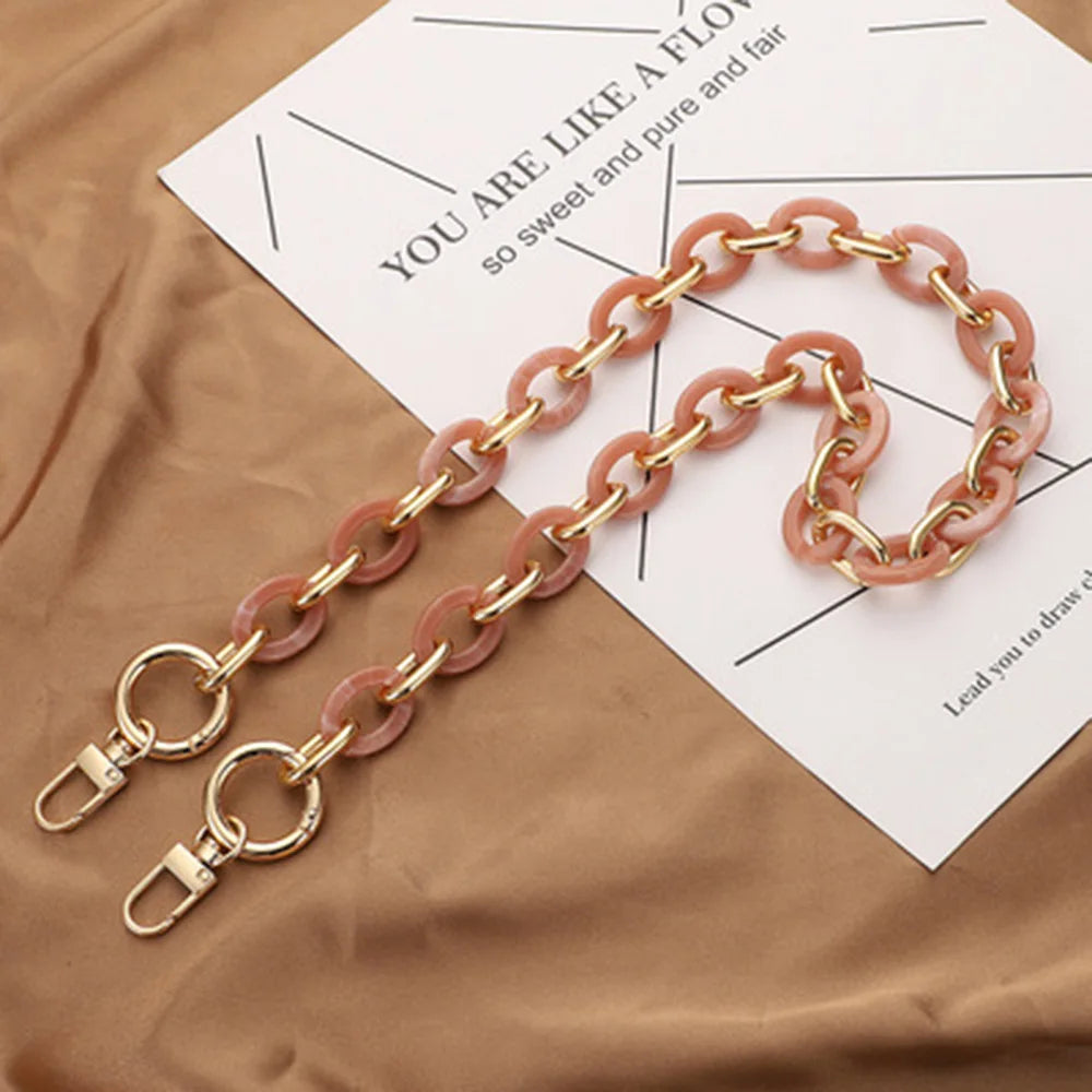 A delicate pink acrylic chain necklace laid on a brown fabric next to a piece of paper.