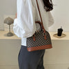 A woman holds a brown leather fashion shell shoulder crossbody bag with a checkered pattern and gold hardware.