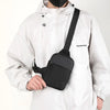 A person wearing a white hooded jacket is holding a black canvas crossbody sling bag.