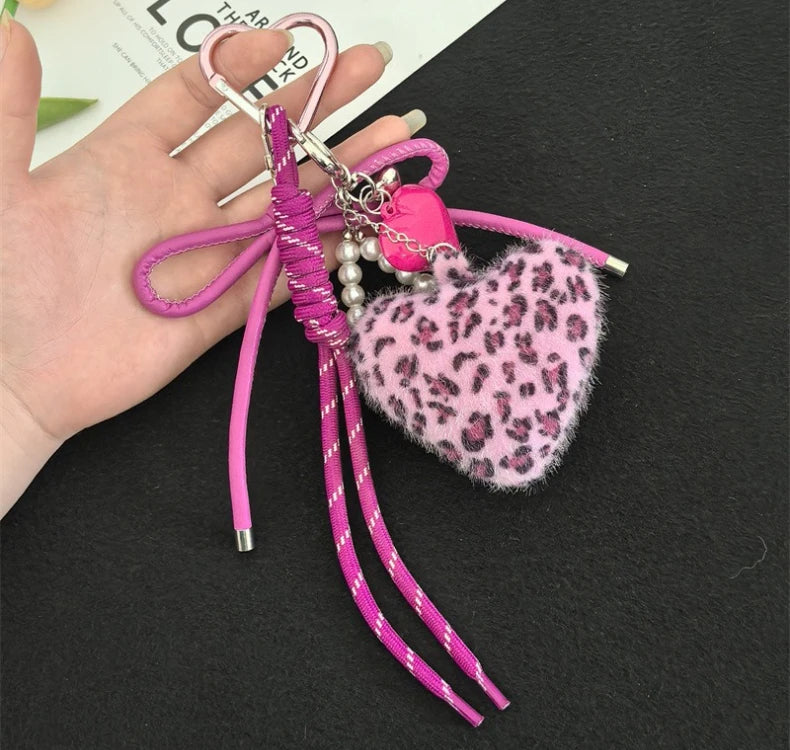 A pink and black leopard print plush heart pendant keychain with pink string and pearl accents.