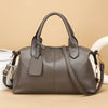 A brown soft leather tote bag with a zipper and adjustable shoulder strap resting on a light surface.