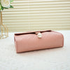 A light pink beaded square crossbody bag resting on a white surface with a blurred floral arrangement in the background.