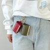 A close-up of a reusable nylon mini keychain tote bag in olive green and red resting on light wash denim fabric.