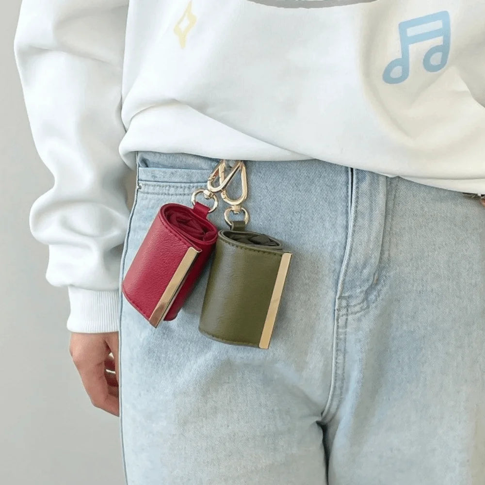 A close-up of a reusable nylon mini keychain tote bag in olive green and red resting on light wash denim fabric.