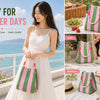 A woman models a white dress and a striped knit bucket tote bag in pink and green against a scenic outdoor background.