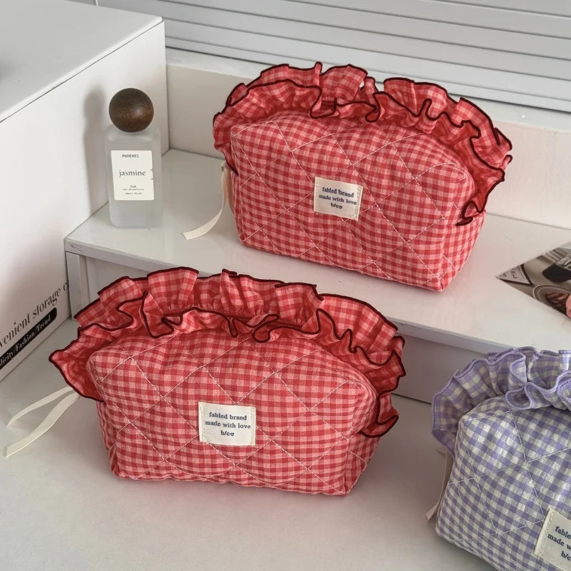 A red and white checkered makeup pouch with lace trim is displayed on a white shelf.