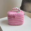 A pink striped Y2K makeup bag with a pink fabric lining and a clear zipper is shown on a white surface.