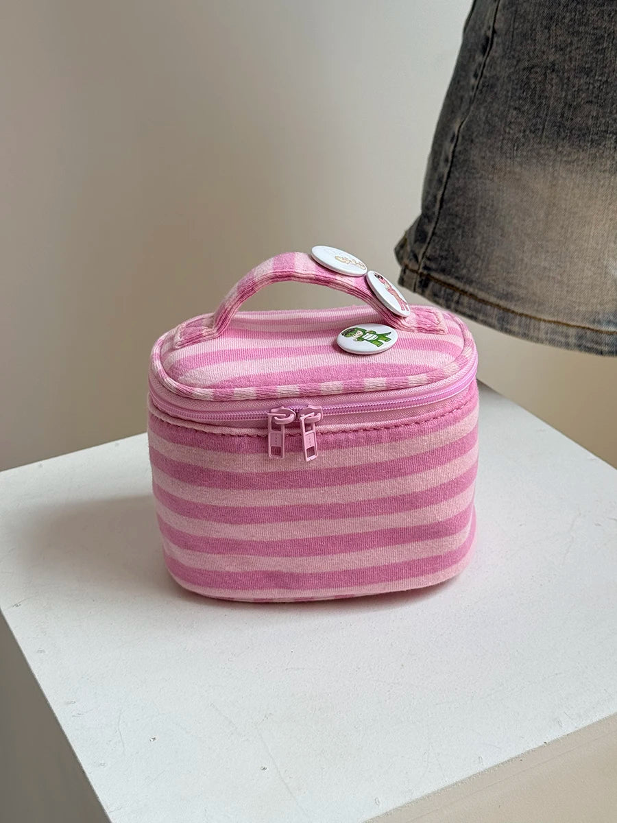 A pink striped Y2K makeup bag with a pink fabric lining and a clear zipper is shown on a white surface.