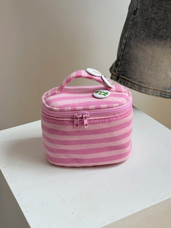 A pink striped Y2K makeup bag with a handle and zipper is shown resting on a white surface.