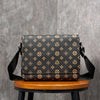 A black and gold patterned men's casual crossbody bag resting on a wooden stool against a gray background.