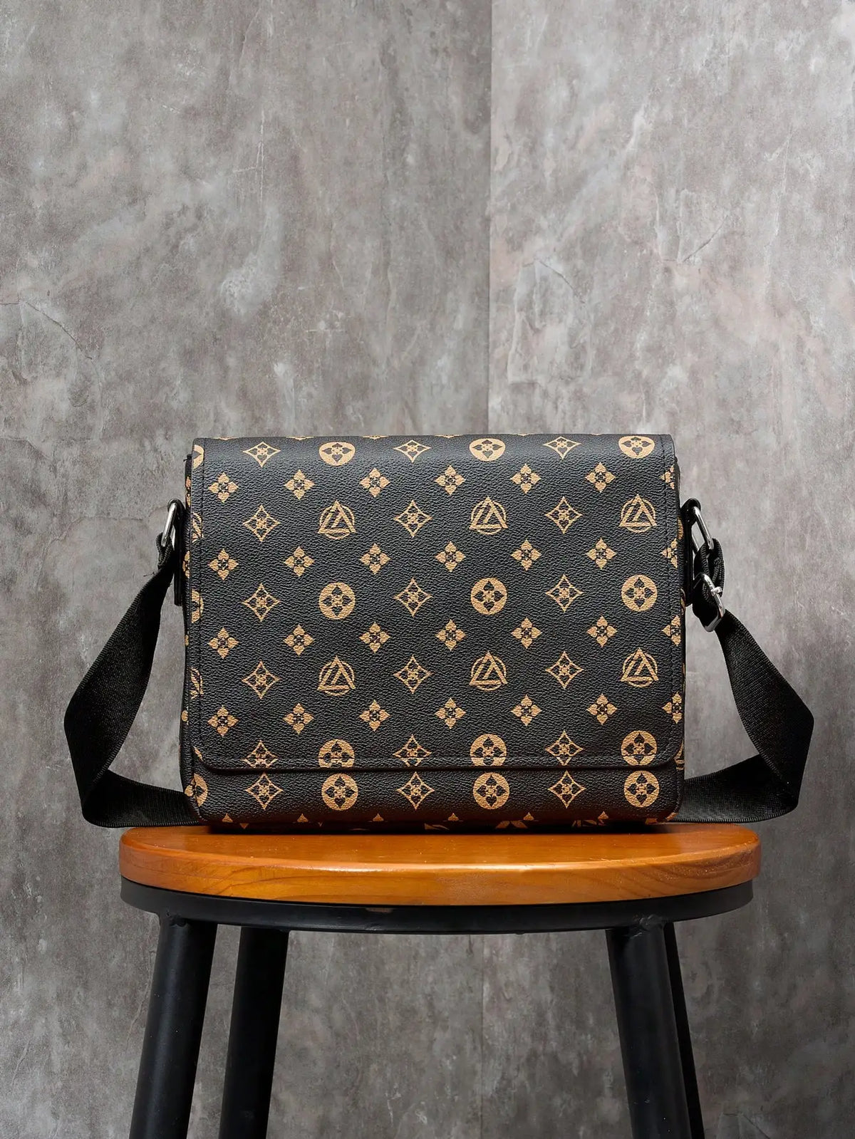 A black and gold patterned men's casual crossbody bag resting on a wooden stool against a gray background.
