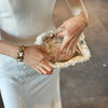 A person holds a white beaded chain shoulder clutch bag in their hand.