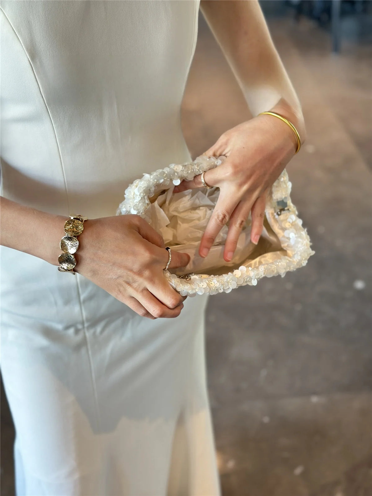 A person holds a white beaded chain shoulder clutch bag in their hand.