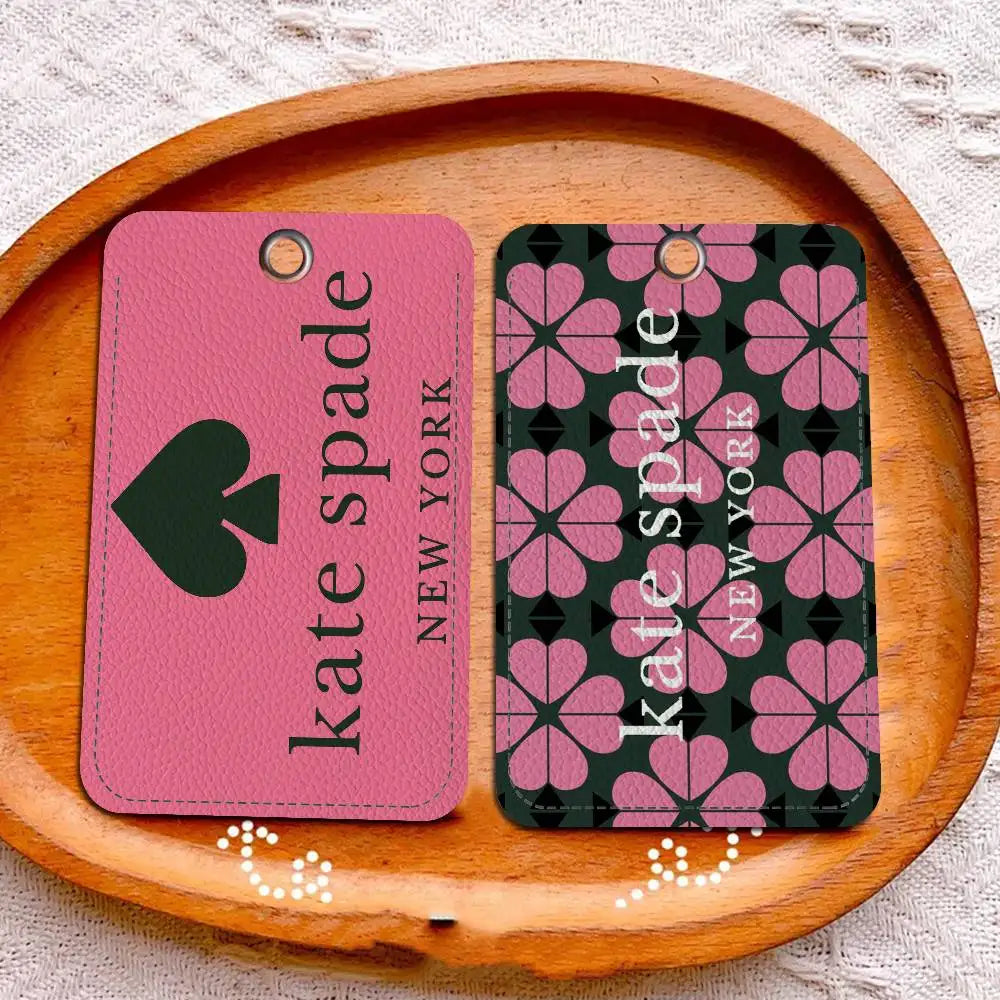 A pink leather card holder with a spade design and a dark green patterned card holder on a wooden board.